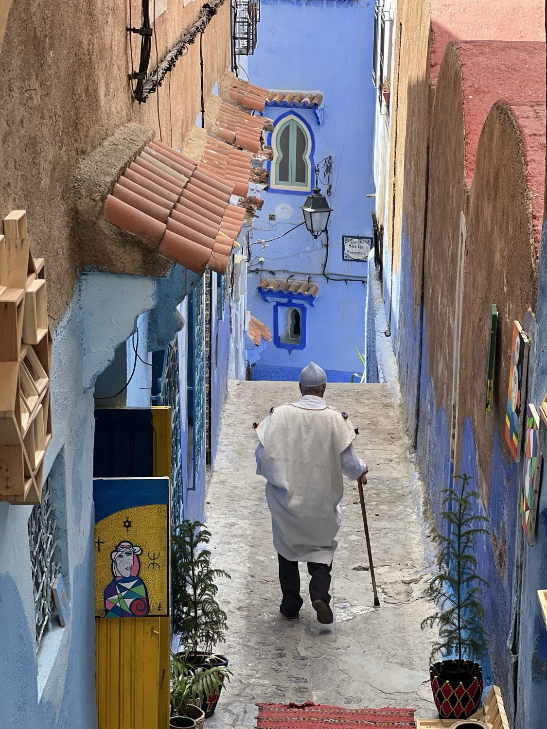 Elderly man in white djellaba with walking stick in a narrow blue-painted alley, Chefchaouen, Morocco