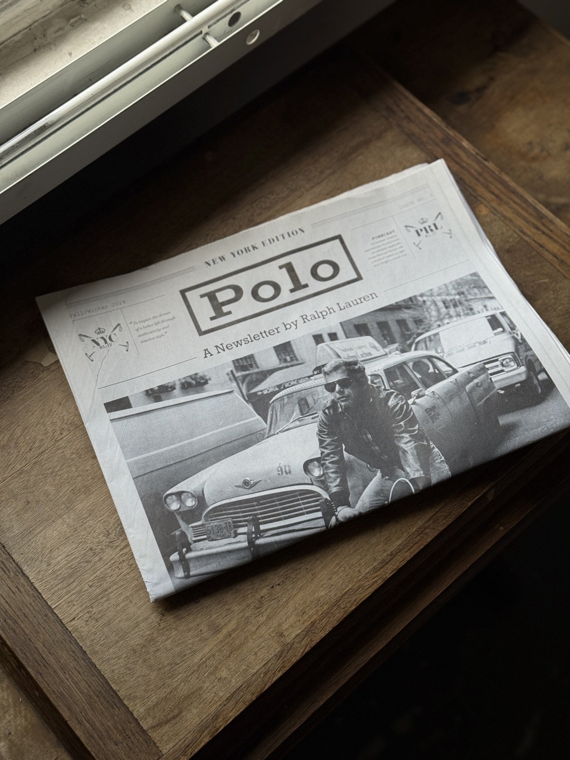 Polo Ralph Lauren newspaper folded on a dark oak table beside a window