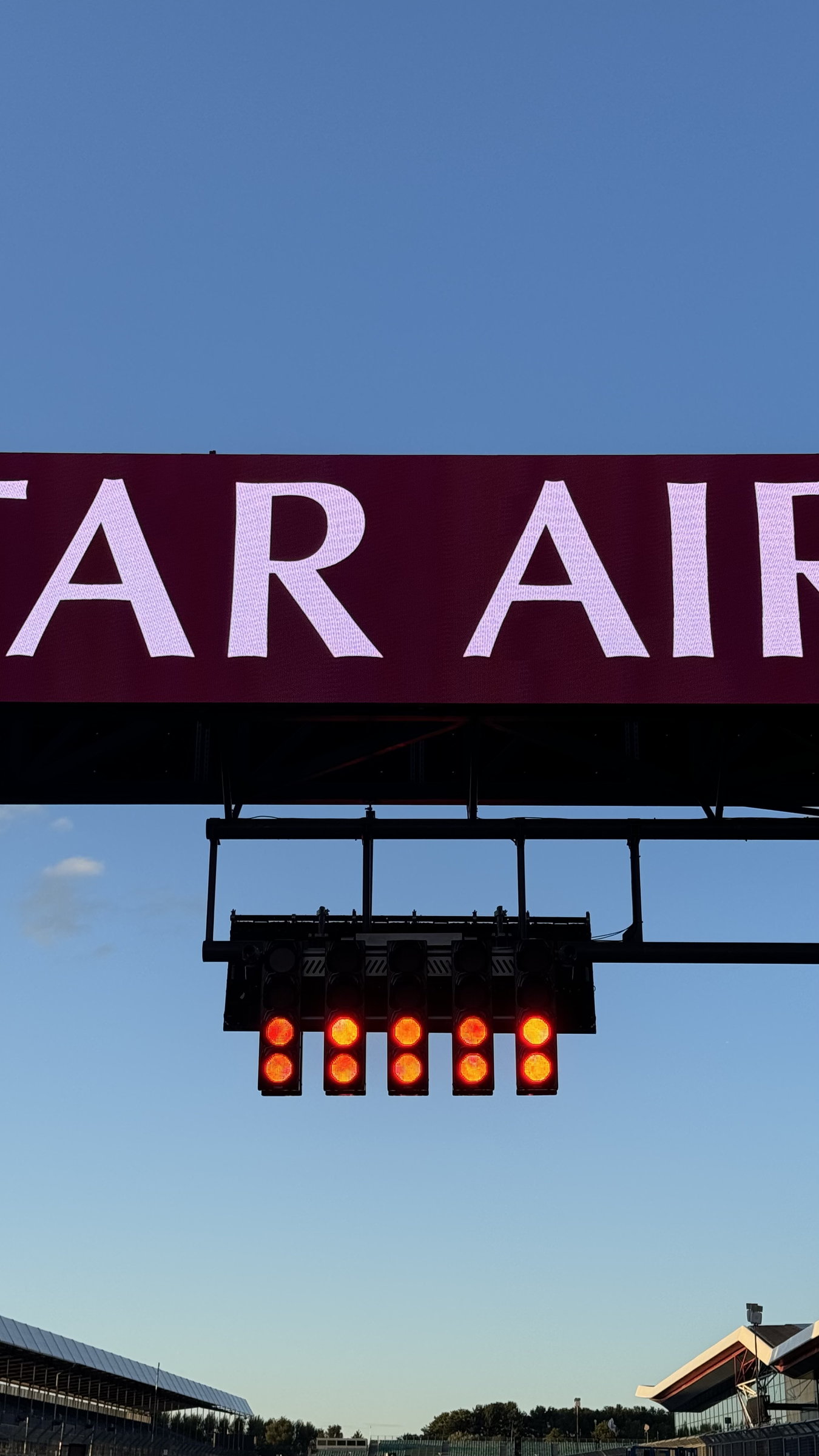 Five race start lights on a circuit gantry against a deep blue sky, Qatar Airways sign above