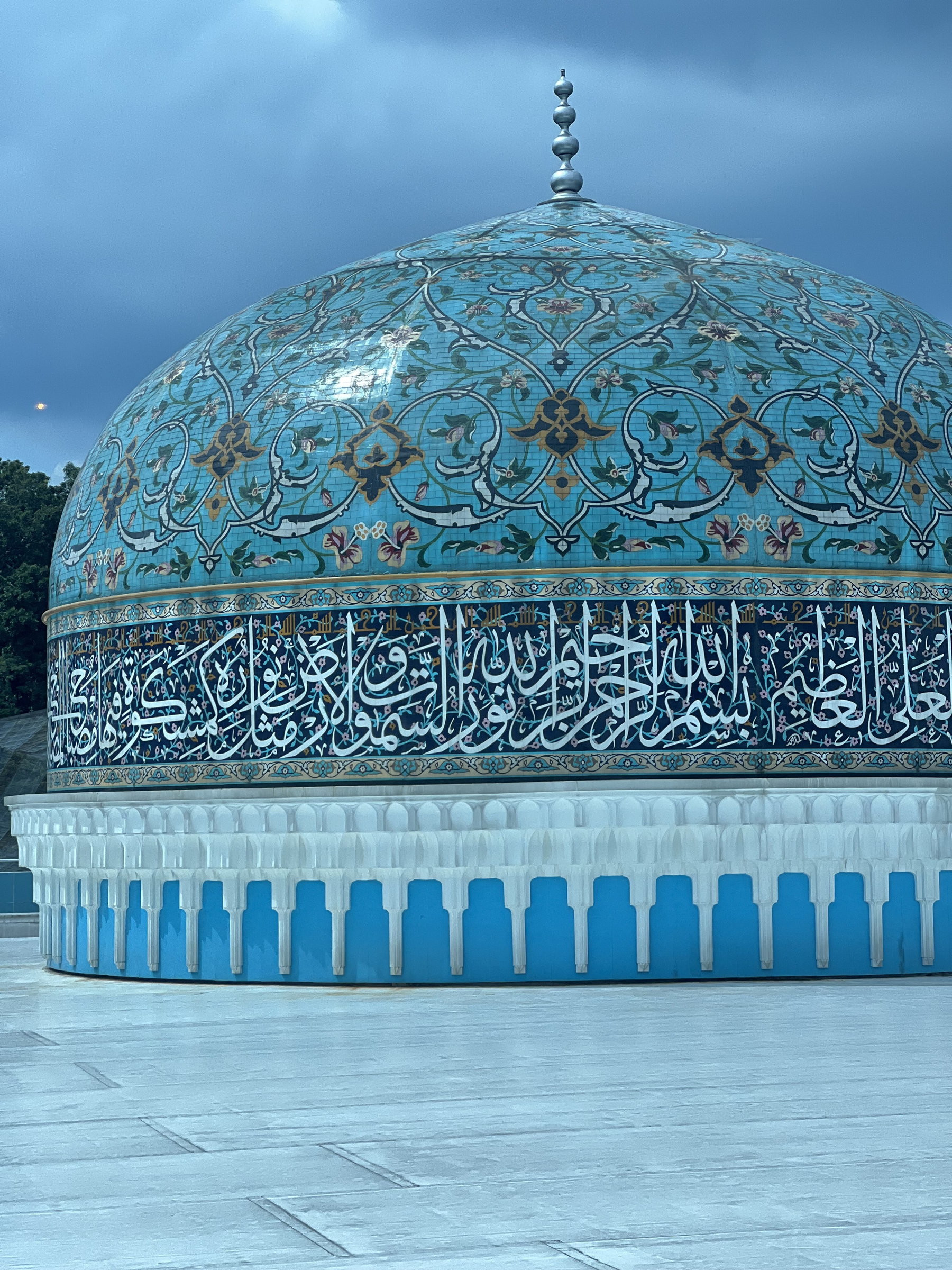 Blue-tiled dome with calligraphic band against a storm sky