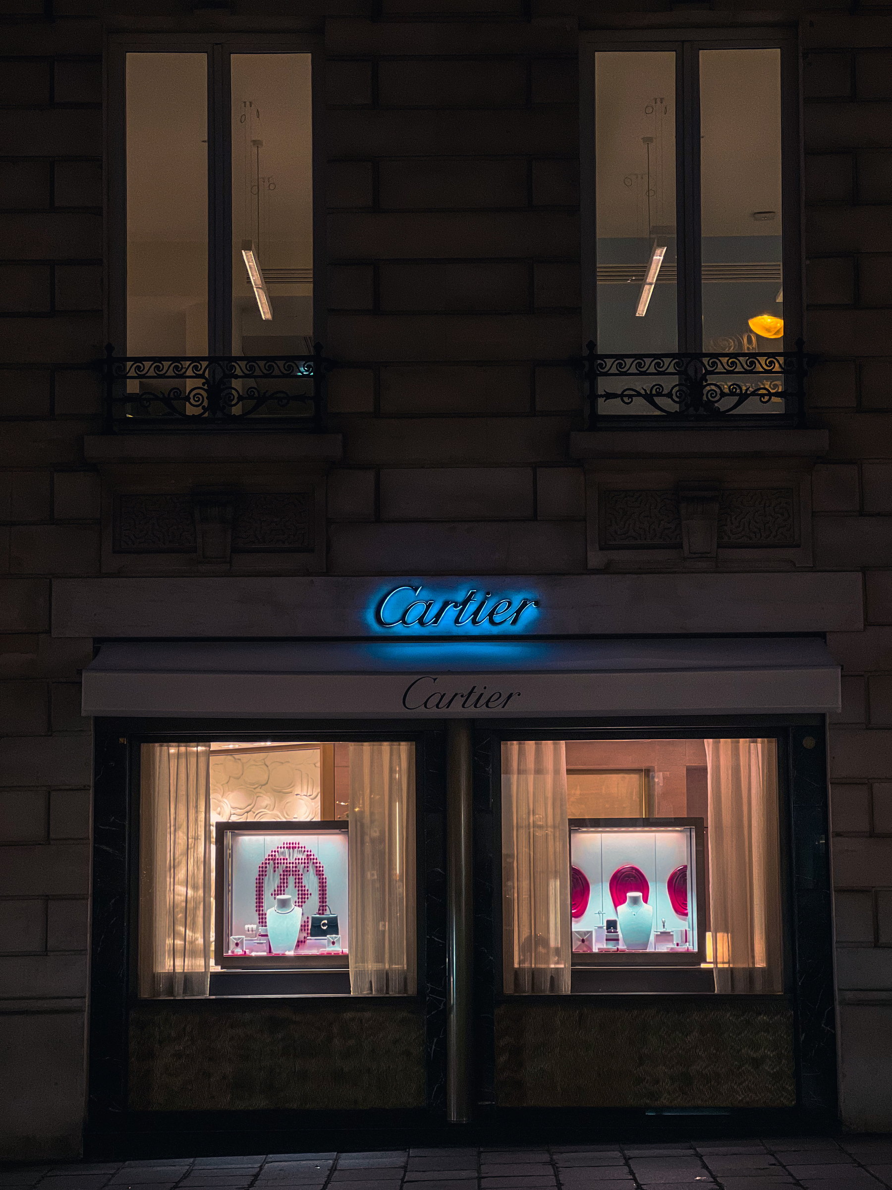 Cartier facade at night, the sign in blue neon above lit vitrines