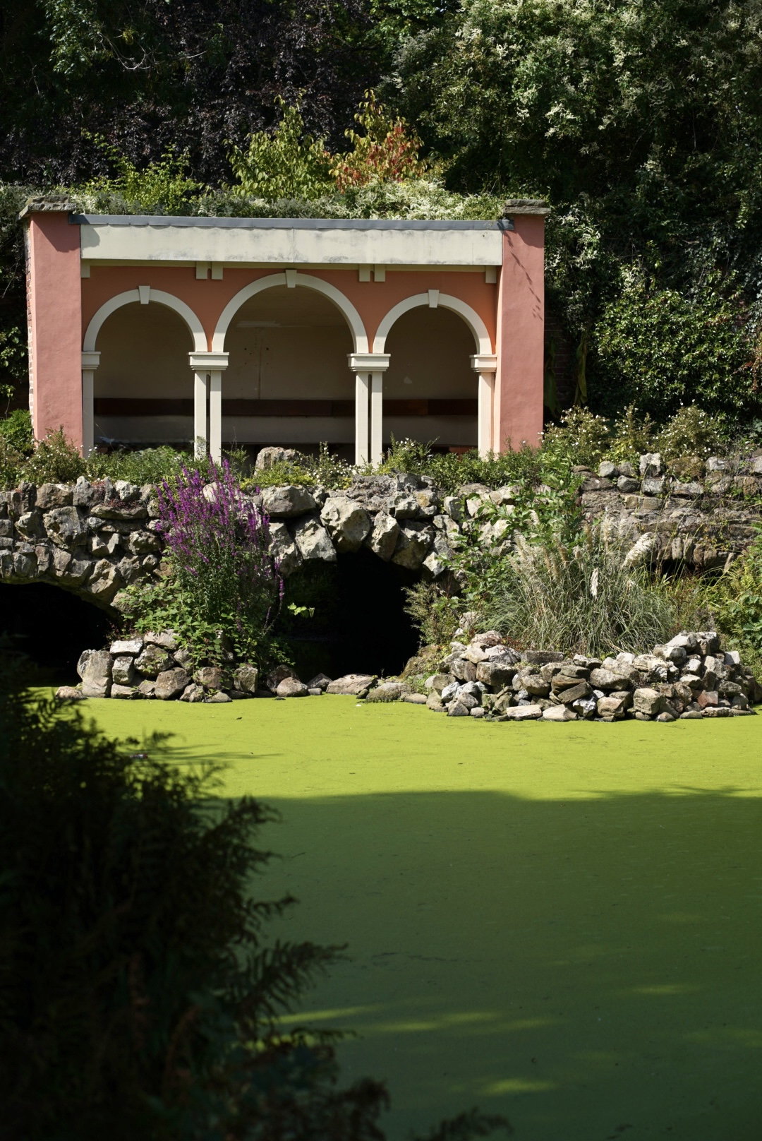 A garden grotto with pink arcaded loggia above still green water