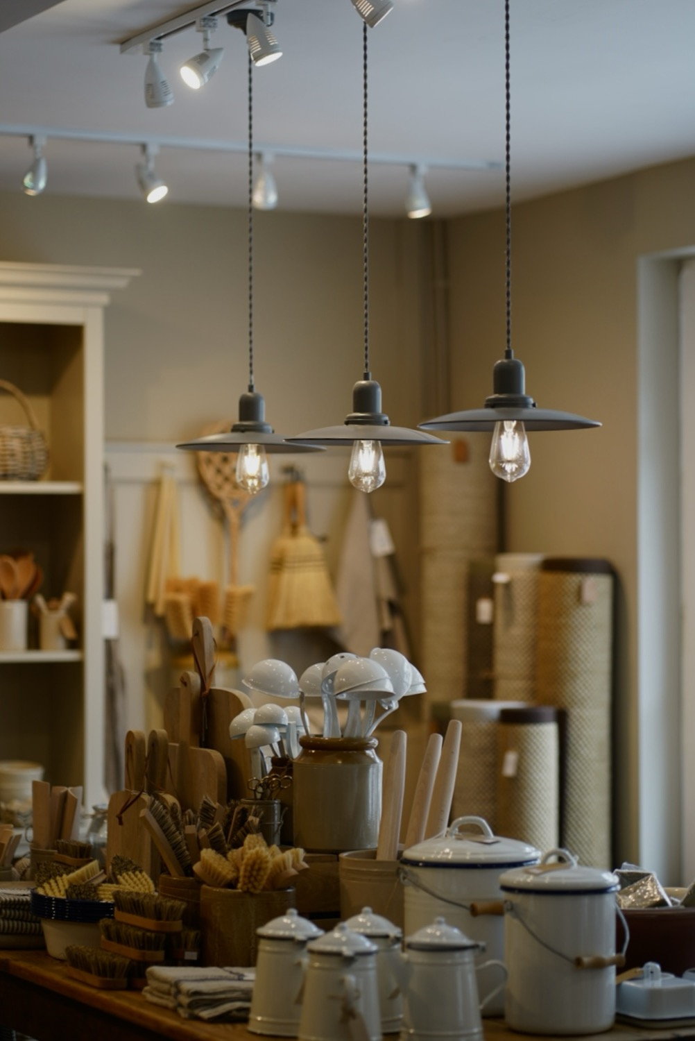 Three pendant lights hanging over a warm shop counter with brushes and homeware
