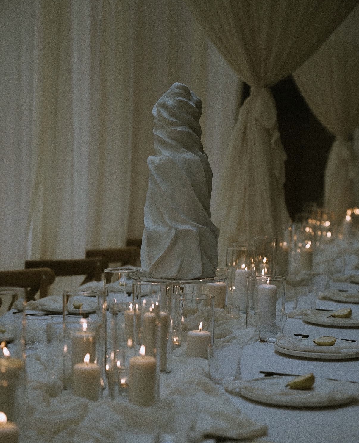 Long candlelit dinner table with white sculptural centrepiece and white draping beyond