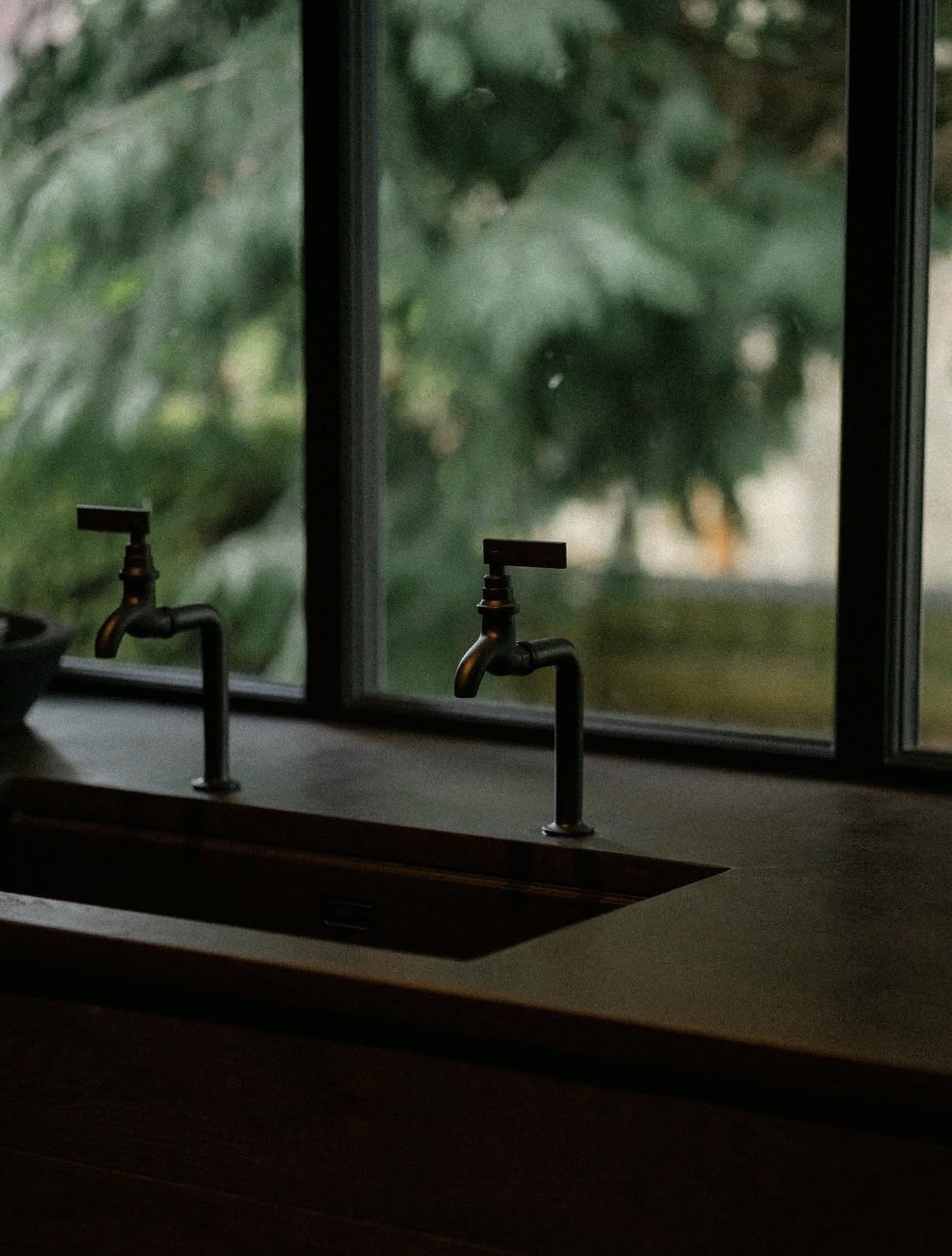 Bronze taps at bar sink with trees visible through window, The Penny Bun, Askwith.