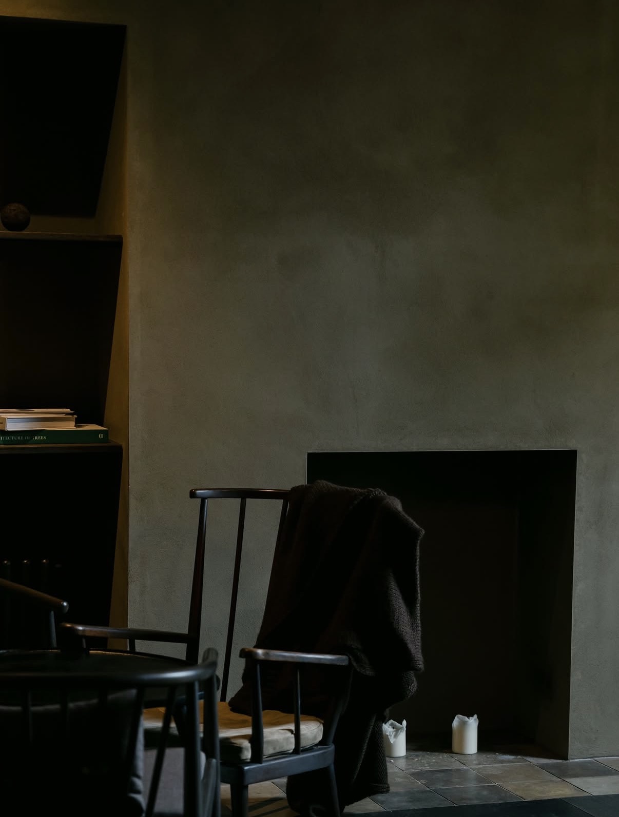 The Penny Bun, Askwith. Clay plaster wall, unlit fireplace, Windsor chair with draped blanket and candles.