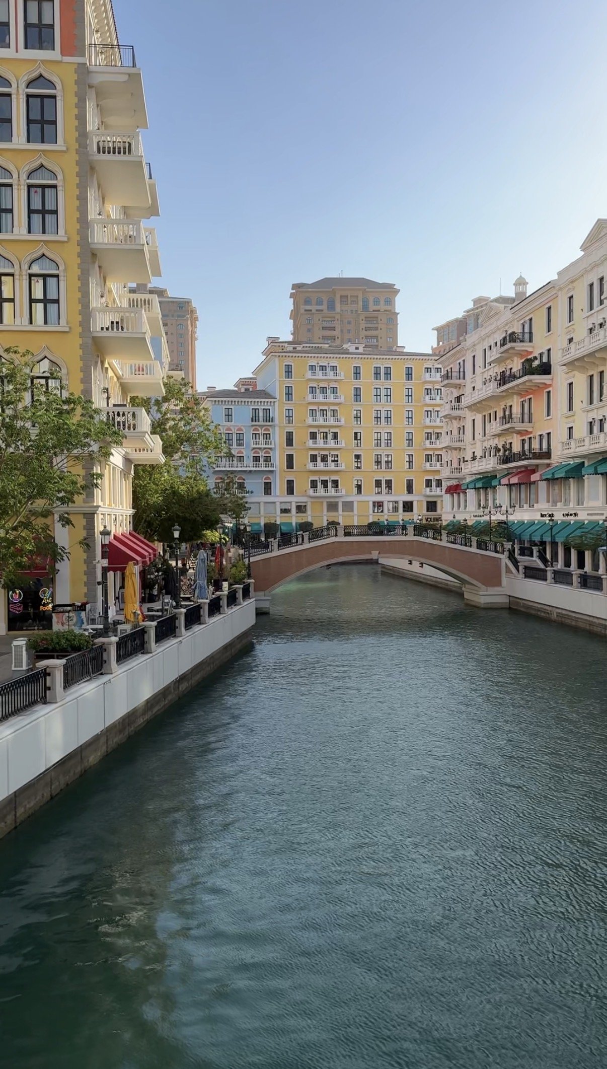 A canal and stone footbridge between pastel facades, Qanat Quartier, The Pearl, Doha
