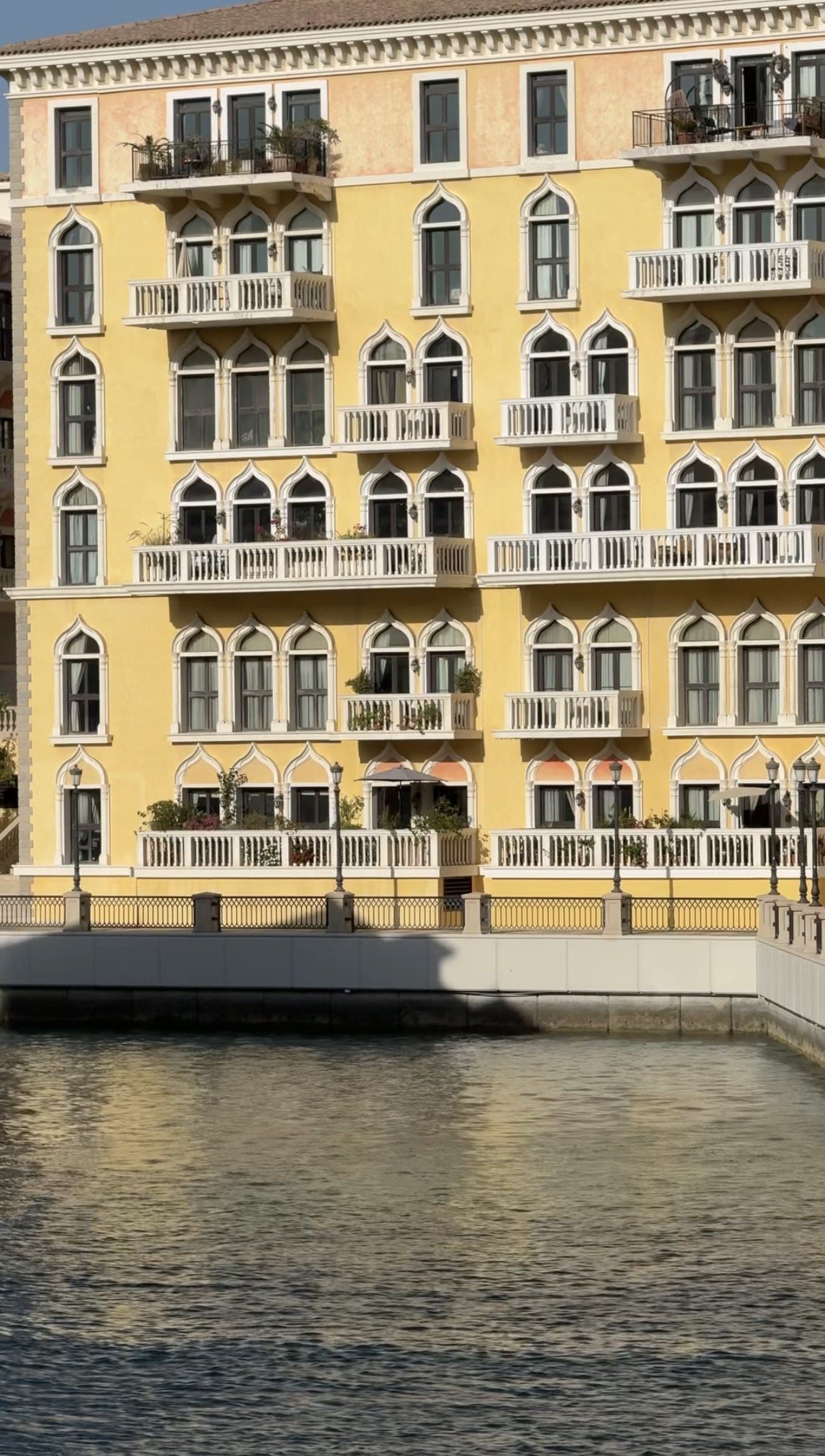 A yellow facade with white balconies above the green water, Qanat Quartier, Doha