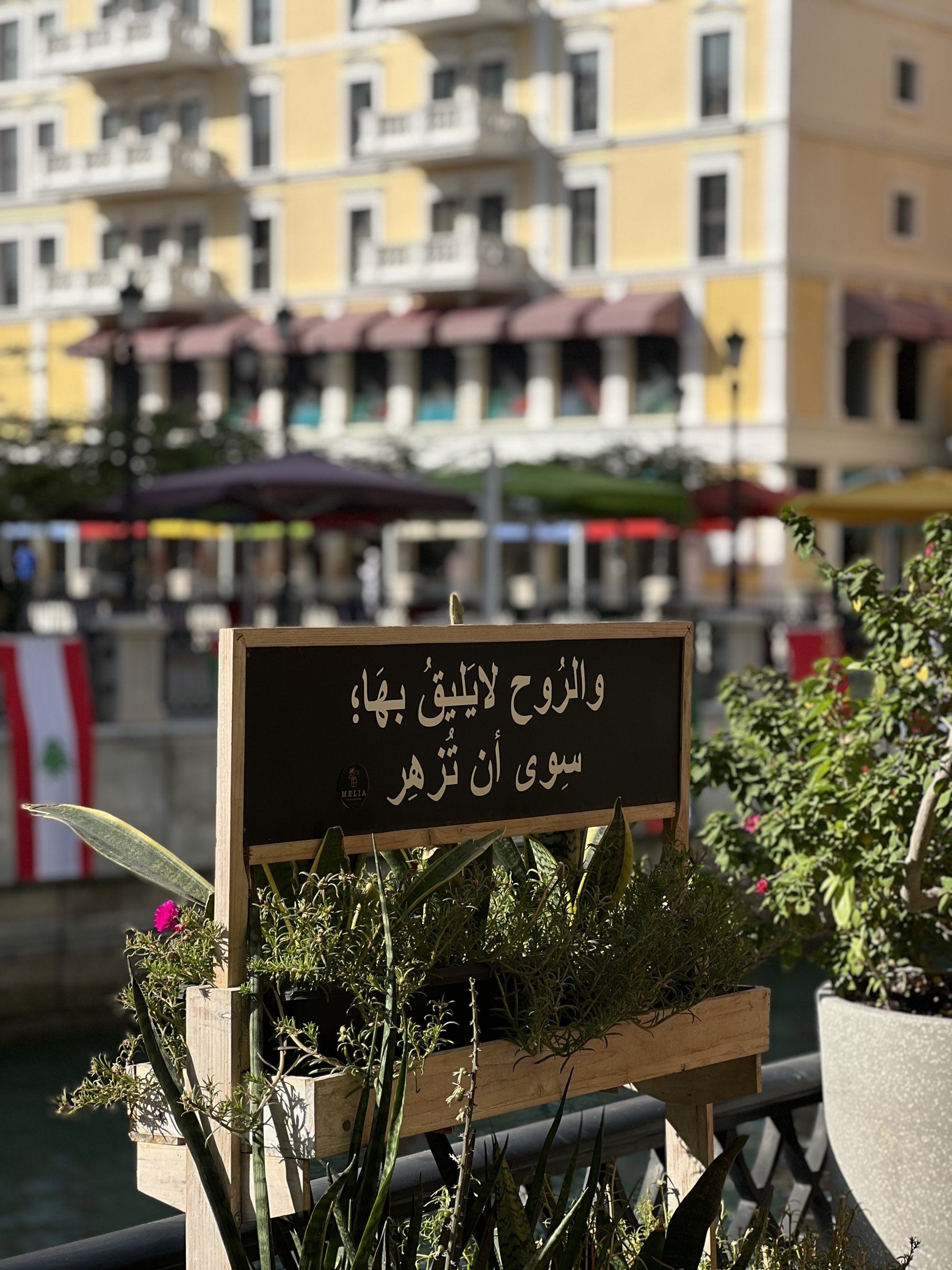 A line of Arabic verse on a sign among café planters, Qanat Quartier, Doha
