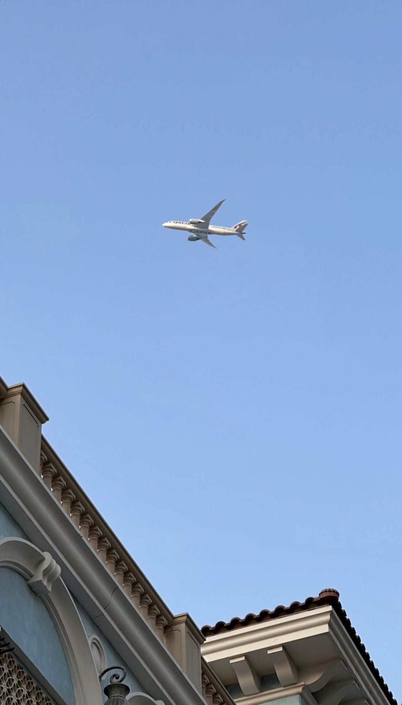 An airliner crossing above a tiled roofline, Qanat Quartier, Doha