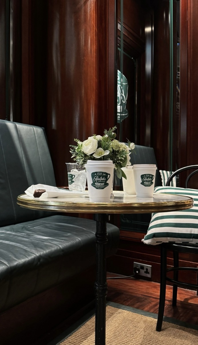 Three Ralph's Coffee takeaway cups on a round table in a dark wood booth with white flowers