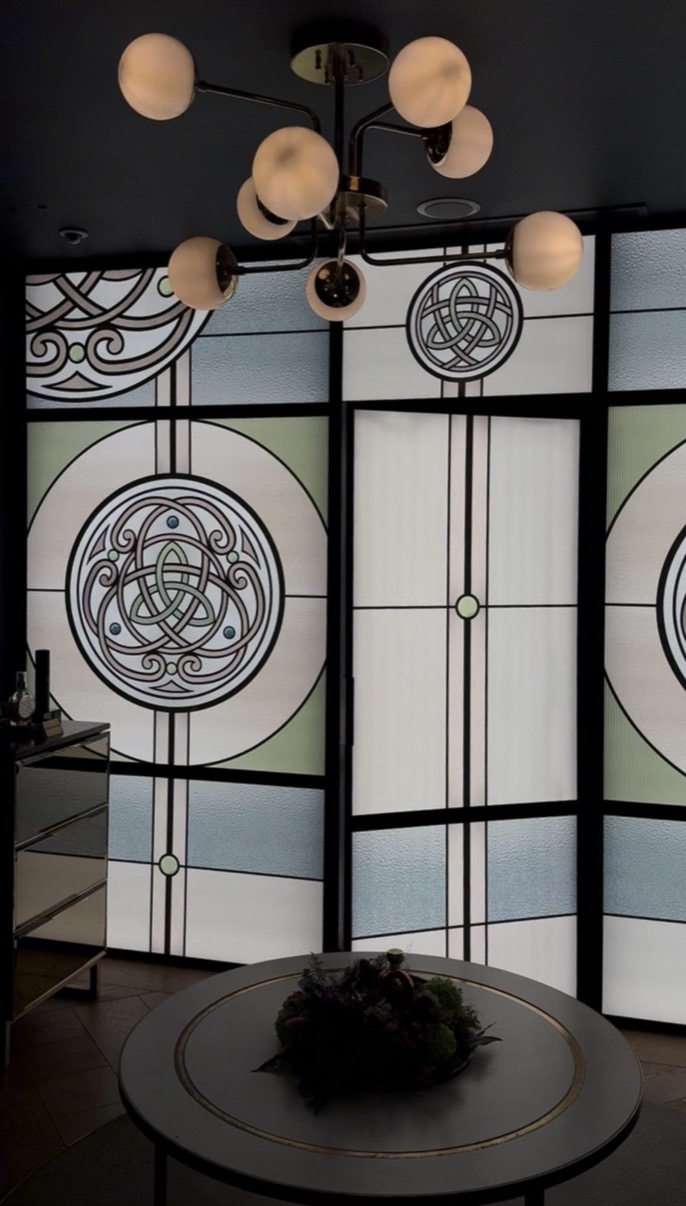 Stained glass screen with art deco medallions and a globe chandelier above a round table, Salon de Parfums, Harrods, London