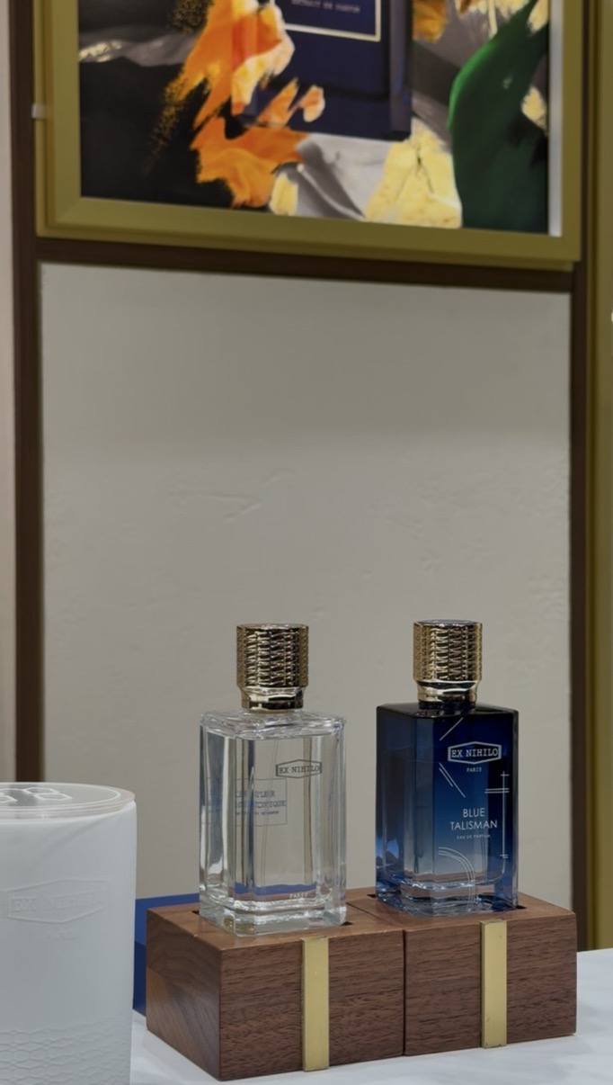 Two Ex Nihilo perfume bottles on a walnut and brass display block with an artwork behind, Salon de Parfums, Harrods, London