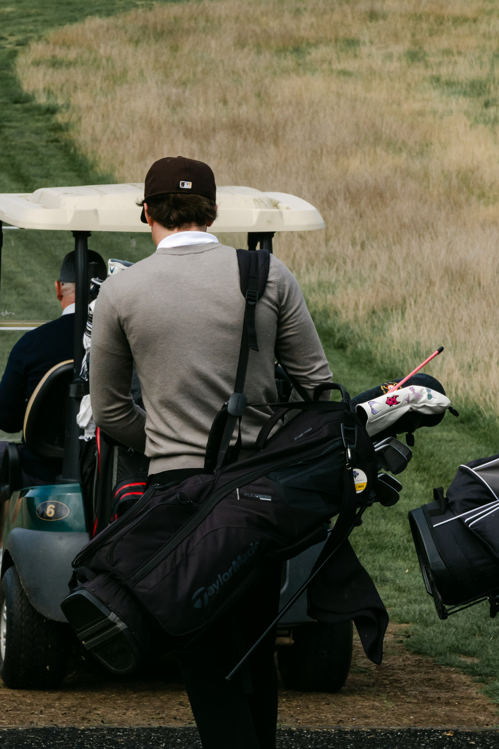 A player carrying his bag past a buggy in the long grass, McLaren Construction Group Golf Day, Kent