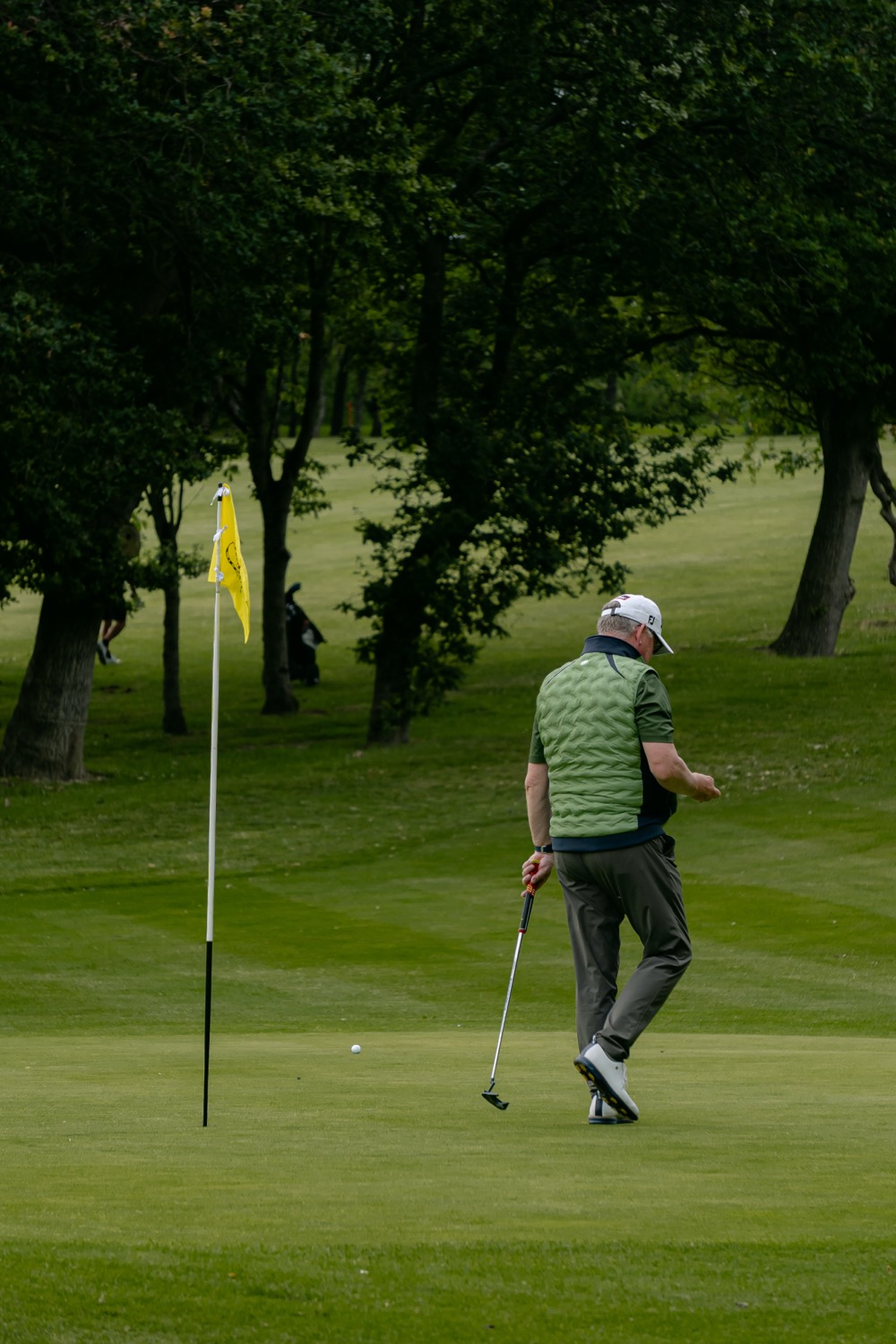 A player crossing the green with a putter as the flag leans in the wind, Magnolia Classic, Horsforth Golf Club, Leeds