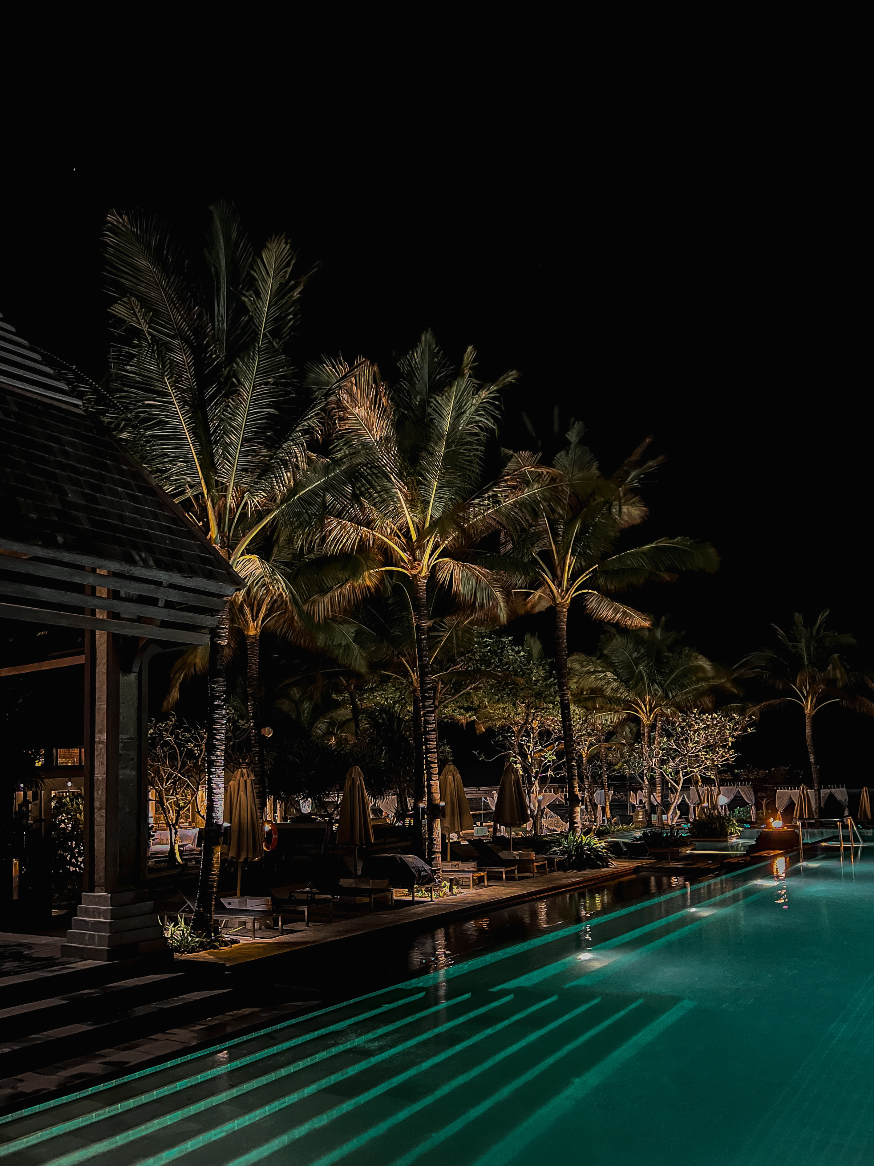 Night pool, palms lit from below, turquoise water, The Ritz-Carlton Bali